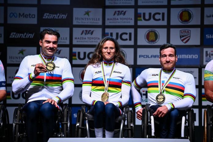 Three Para cyclists wearing the iconic UCI rainbow jersey smile with their gold medals